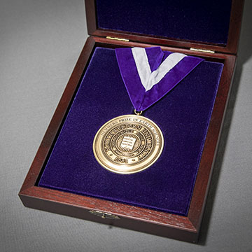 A round gold medal on a purple ribbon in a black velvet-lined box.